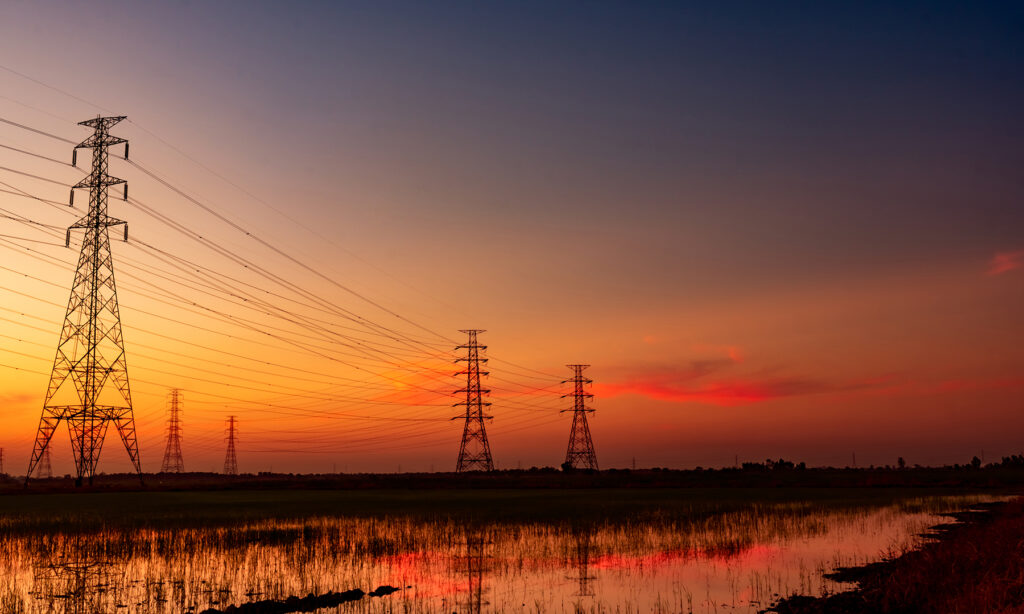 High Voltage Electric Pylon And Electrical Wire With Sunset Sky.